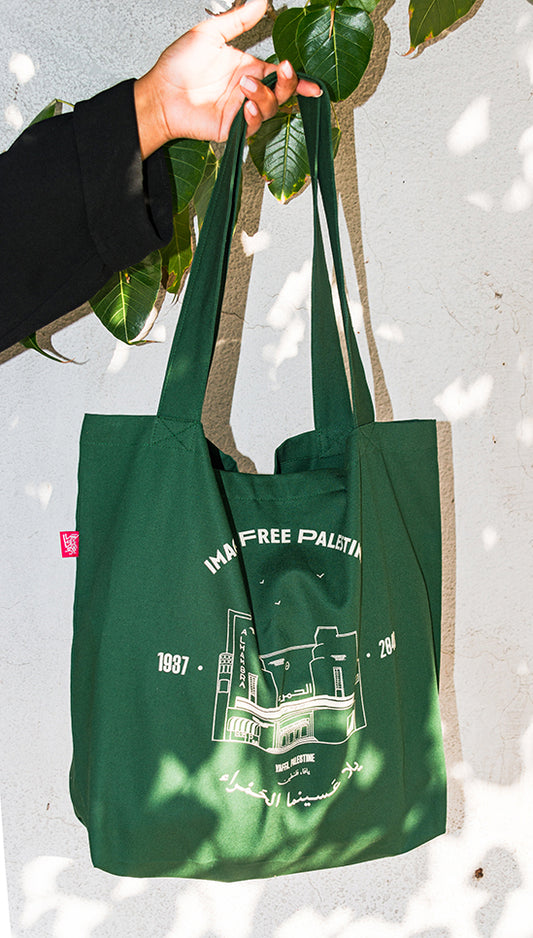 "Illustration of an exclusive tote paying tribute to the Alhambra Cinema in Yaffa, Palestine, with the text 'Imagine a Free Palestine.' Product details: 100% Cotton, 50cm x 40cm x 6cm, screen printed design, with a middle pocket for added utility. Support a free Palestine with your purchase."